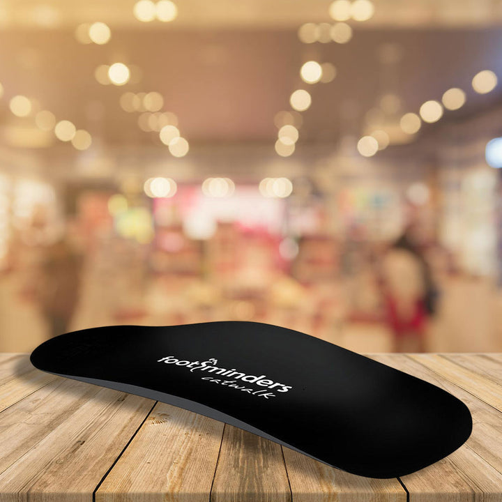 Black insole with 'footminders' logo on a wooden surface, blurred store background