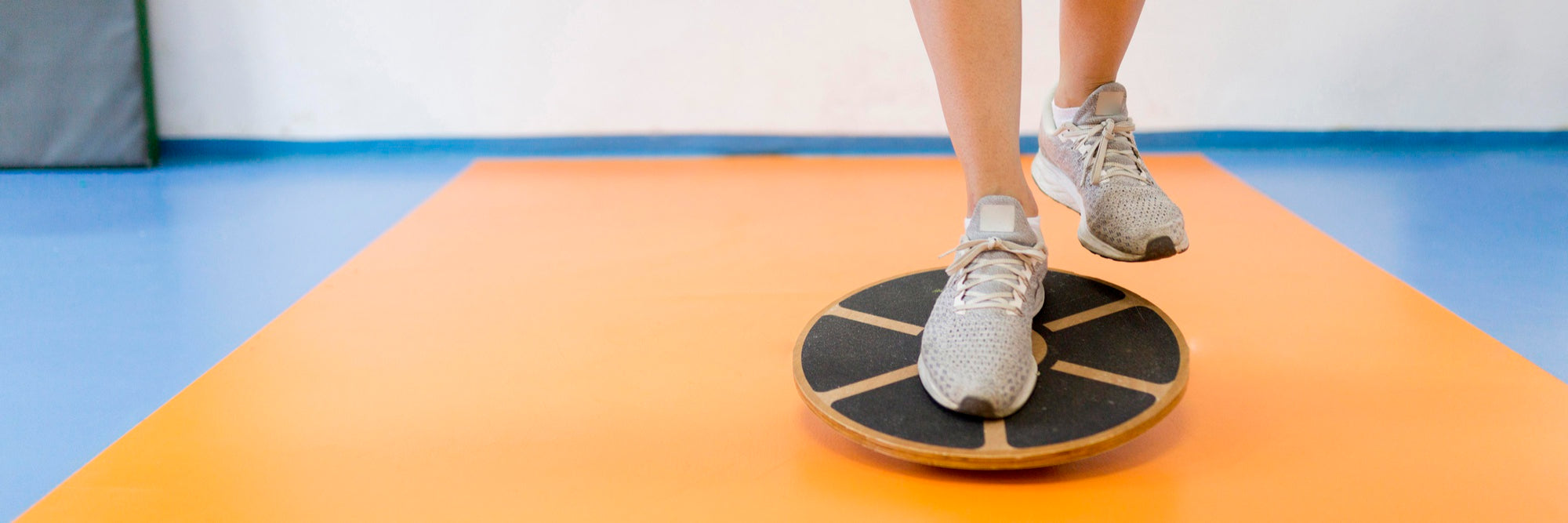 Person using a balance board on an orange and blue mat